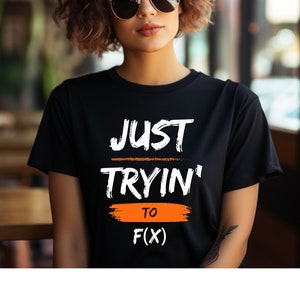 May include: Black t-shirt with white text that reads "JUST TRYIN' TO F(X)". The text is in a handwritten style with an orange line under "TRYIN'" and an orange brushstroke under "TO".