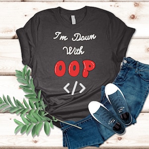 Könnte beinhalten: Dunkelgraues T-Shirt mit dem Text "I'm Down With OOP" in Weiß und Rot. Das Shirt wird mit einer blauen Jeans und marineblauen Turnschuhen mit weißen Sohlen kombiniert. Ein Zweig mit grünen Blättern ist seitlich platziert.