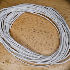 Puede incluir: Un rollo de cordón o cuerda blanco, probablemente utilizado para manualidades o la elaboración de joyas.