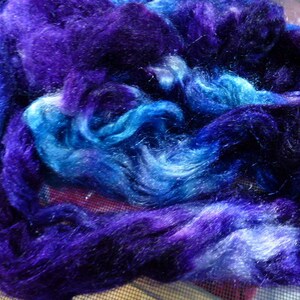 Pu&ograve; includere: Primo piano di un mucchio di filato blu e viola. Il filato &egrave; morbido e soffice, e ha una finitura scintillante.