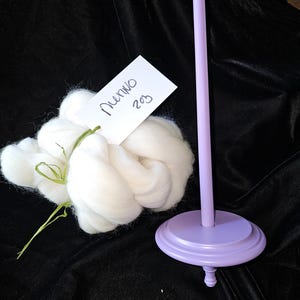 May include: A lavender colored spinning wheel with a white ball of wool. The wool is labeled "Merino 203".