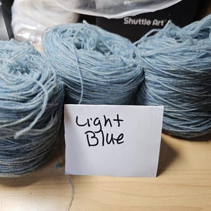 Puede incluir: Tres ovillos de hilo azul claro, etiquetados como "Light Blue".