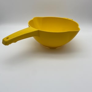 May include: A bright yellow plastic scoop with a handle. The scoop has a rounded bowl shape with a scalloped edge. The handle has a hole at the end for hanging. The scoop is likely for kitchen or garden use.