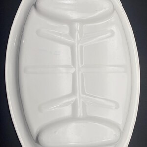 Puede incluir: Plato de servir ovalado blanco con una secci&oacute;n central elevada y dos peque&ntilde;as hendiduras a cada lado. La secci&oacute;n central tiene un dise&ntilde;o elevado con m&uacute;ltiples crestas.