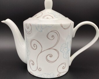 May include: White teapot with a floral design in brown and blue. The teapot has a lid and a handle.