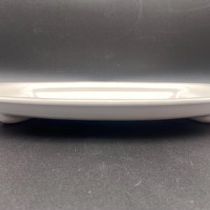 Puede incluir: Plato ovalado blanco para servir con un dise&ntilde;o floral azul alrededor del borde. El plato tiene tres peque&ntilde;os pies en la parte inferior.