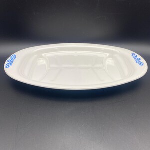 Puede incluir: Plato de servir ovalado blanco con un dise&ntilde;o floral azul alrededor del borde. El plato tiene una secci&oacute;n central elevada y dos secciones m&aacute;s peque&ntilde;as a cada lado.