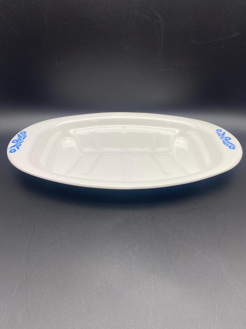 Puede incluir: Plato de servir ovalado blanco con un dise&ntilde;o floral azul alrededor del borde. El plato tiene una secci&oacute;n central elevada y dos secciones m&aacute;s peque&ntilde;as a cada lado.