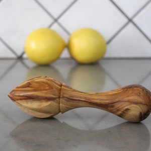 May include: A wooden lemon reamer with a natural wood finish. The reamer has a pointed end for squeezing lemons and a handle for easy gripping.
