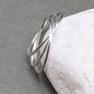 May include: A silver-colored ring featuring a multi-band design with three thin, smooth, interconnected circular loops that overlap to create a layered appearance. The metal has a polished, reflective finish and a rounded, slender profile.