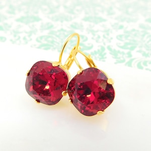 May include: A pair of gold hoop earrings with red square-shaped crystal stones.