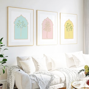 Puede incluir: Tres impresiones enmarcadas con marcos dorados, cada una con un &aacute;rbol estilizado en un arco pastel. Las impresiones est&aacute;n colgadas en una pared blanca sobre un sof&aacute; blanco con almohadas blancas y una manta blanca.