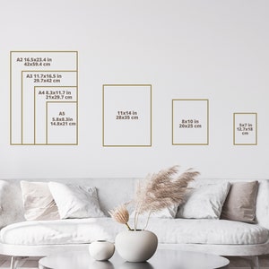May include: A white couch with pillows in a living room with a white wall. The wall has a chart showing different sizes of paper prints in inches and centimeters. The sizes include 16.5x23.4 inches, 11.7x16.5 inches, 8.3x11.7 inches, 5.8x8.3 inches, 11x14 inches, 8x10 inches, and 5x7 inches.