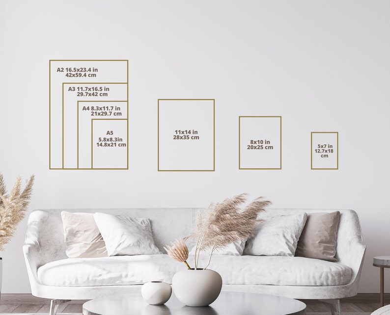 May include: A white couch with pillows in a living room with a white wall. The wall has a chart showing different sizes of paper prints in inches and centimeters. The sizes include 16.5x23.4 inches, 11.7x16.5 inches, 8.3x11.7 inches, 5.8x8.3 inches, 11x14 inches, 8x10 inches, and 5x7 inches.
