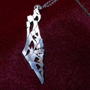 Puede incluir: Un collar con un colgante de plata con forma del contorno de Israel, con letras hebreas recortadas en el diseño.