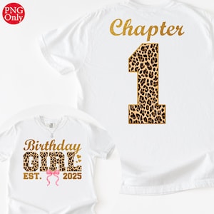 Può includere: T-shirt bianche con testo glitterato dorato e dettagli animalier. Una maglietta dice "Capitolo 1" sul retro. L'altra dice "Birthday Girl" con "EST. 2025" e un fiocco rosa.