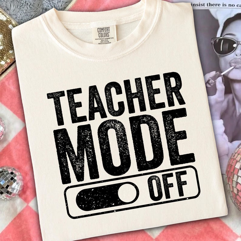 May include: Cream-colored t-shirt with the words "TEACHER MODE OFF" in bold, black, distressed font. The design includes an on/off switch graphic. The shirt is made by Comfort Colors.