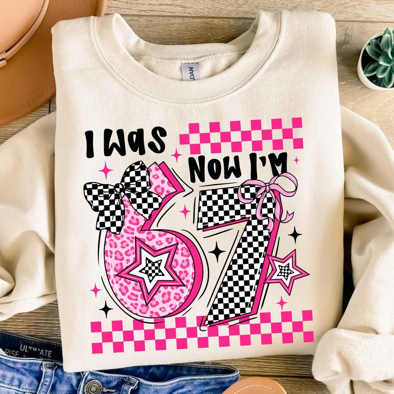 May include: Cream-coloured sweatshirt with the text "I WAS NOW I'M 57". The number 57 is in pink with a leopard print design and a checkered bow. The design includes stars and a checkered pattern.