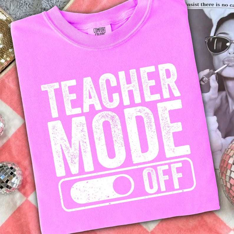 May include: A pink sweatshirt with the words "TEACHER MODE OFF" printed in white. The text is in a bold, sans-serif font. The sweatshirt has a crew neck and long sleeves. The Comfort Colors logo is visible on the collar.