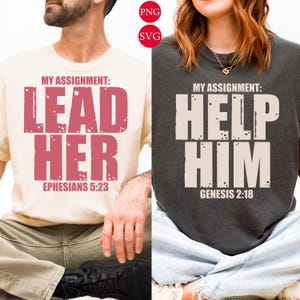 May include: Two t-shirts, one cream and one charcoal grey, each featuring a striking text design. The cream shirt displays "MY ASSIGNMENT: LEAD HER EPHESIANS 5:23" in red. The grey shirt reads "MY ASSIGNMENT: HELP HIM GENESIS 2:18" in white.