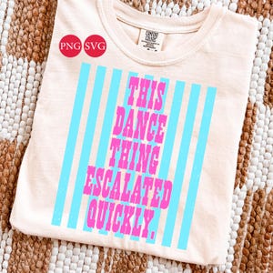 May include: A light peach-colored t-shirt with the text "THIS DANCE THING ESCALATED QUICKLY" in pink, framed by vertical blue stripes. The shirt has a crew neck and short sleeves. The shirt is made by Comfort Colors.