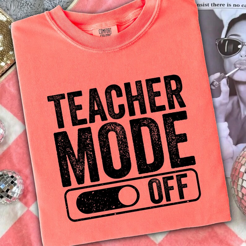 May include: Coral-colored sweatshirt with the words "TEACHER MODE OFF" printed in black. The text is in a bold, sans-serif font. The sweatshirt has a crew neck and long sleeves. The image also includes a sequined bag and a disco ball.