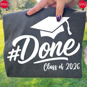 May include: Dark gray t-shirt with the word "#Done" in a white script font, a white graduation cap graphic, and the text "Class of 2026". The shirt is held up by a person.