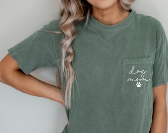 May include: A moss green t-shirt with a pocket that says "dog mom" in white script with a white paw print.