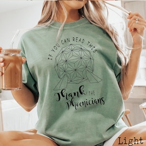 Puede incluir: Una camiseta verde claro con un gráfico negro de la atracción Spaceship Earth en Epcot. El texto "If you can read this thank the Phoenicians" está impreso en la camiseta.