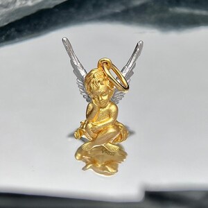 K&ouml;nnte beinhalten: Ein goldener Cherub-Anh&auml;nger mit silbernen Fl&uuml;geln. Der Cherub sitzt mit gefalteten H&auml;nden und hat einen Heiligenschein. Der Anh&auml;nger hat oben eine Schlaufe zum Anbringen an einer Halskette oder einem Armband.