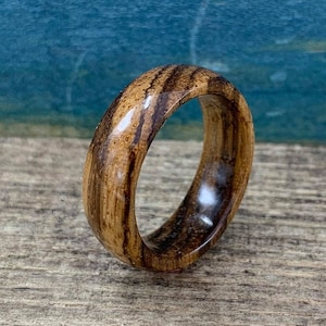 May include: A wooden ring with a dark brown and light brown striped pattern. The ring is smooth and polished.