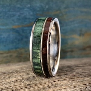 May include: A silver ring with a green and brown wood inlay. The ring has a silver band with a thin silver wire wrapped around the wood inlay.