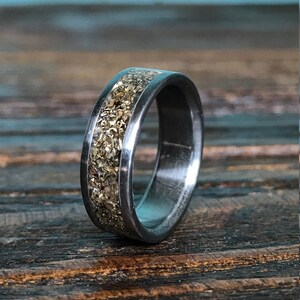 A close-up shot of a dark metallic ring showing a speckled, glittering gold inlay running along its center.