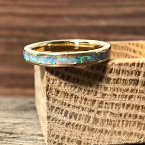 A gold ring with an opal inlay sits on the corner of a small wooden block.