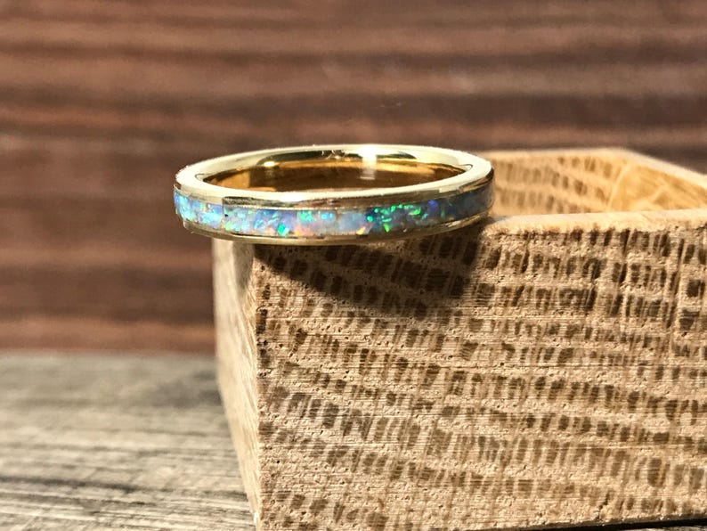 A gold ring with an opal inlay sits on the corner of a small wooden block.
