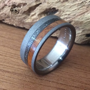 May include: A gray titanium ring with a brown wood inlay and a black stripe. The ring has a brushed finish.