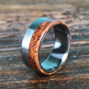 May include: A silver and brown wood ring with a brushed finish. The ring has a wide band with a thin silver strip around the edge.