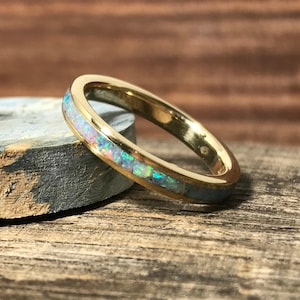 A thin gold ring with an opal inlay rests against a textured blue and grey stone on a wooden surface.