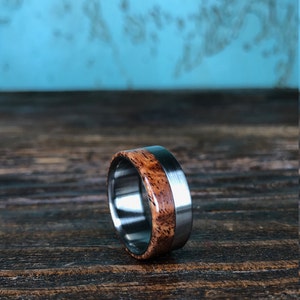May include: A brown wood and silver metal ring. The ring has a wide band with a thin silver metal band around the edge of the wood.