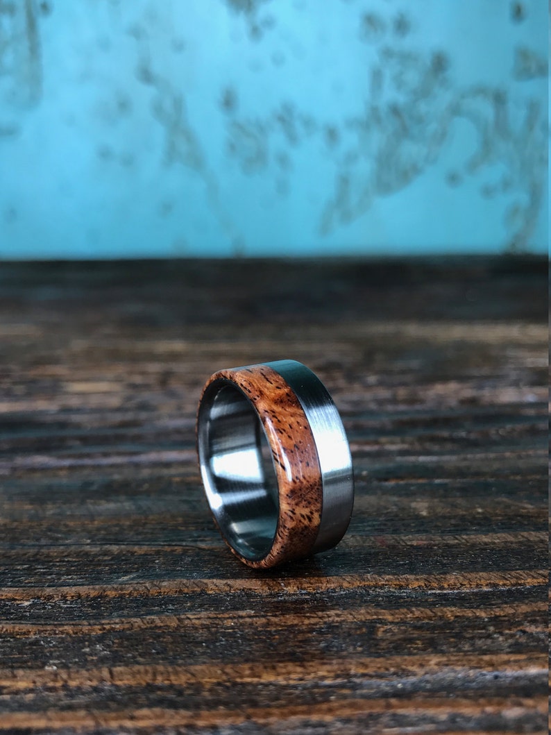 May include: A brown wood and silver metal ring. The ring has a wide band with a thin silver metal band around the edge of the wood.
