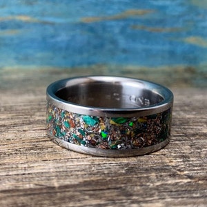 Pu&ograve; includere: Un anello in titanio argentato con un'incisione macchiettata di verde, marrone e oro.