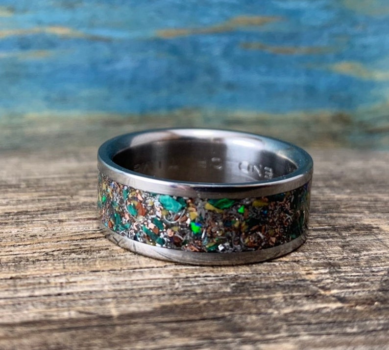 Pu&ograve; includere: Un anello in titanio argentato con un'incisione macchiettata di verde, marrone e oro.