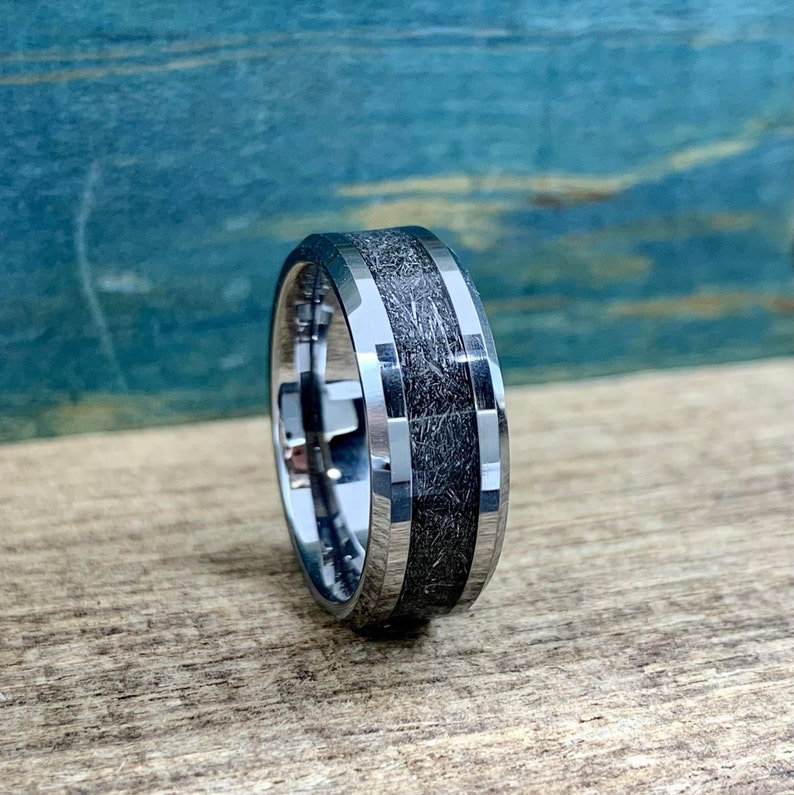 May include: A silver tungsten carbide ring with a black inlay. The inlay has a textured, wood-like pattern.