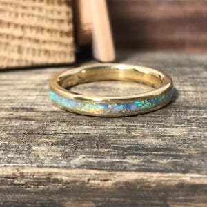 A gold ring with a sparkling opal inlay is displayed on a weathered wooden plank.
