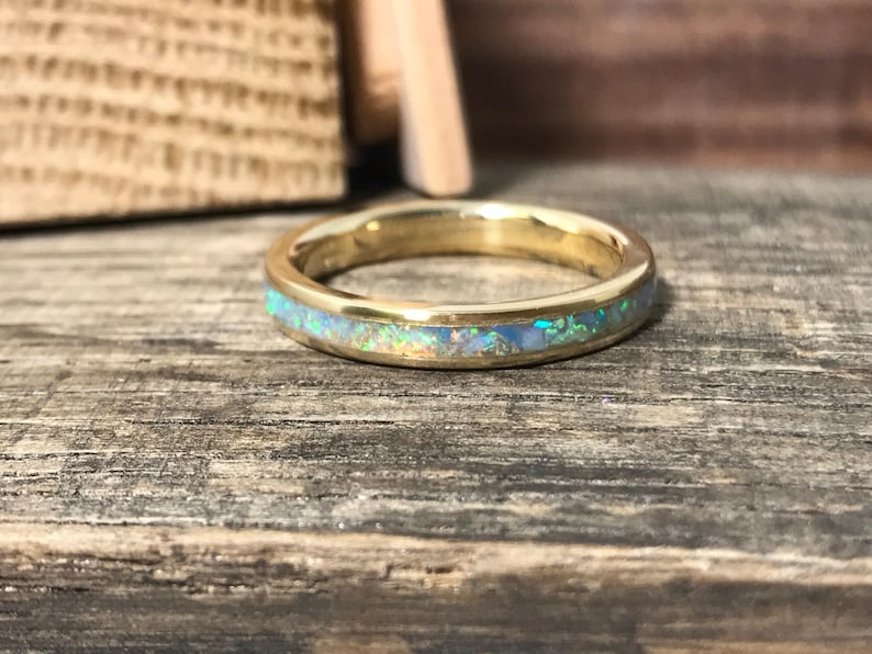 A gold ring with a sparkling opal inlay is displayed on a weathered wooden plank.