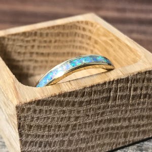 A gold ring with an opal inlay is placed inside a small, open wooden box.