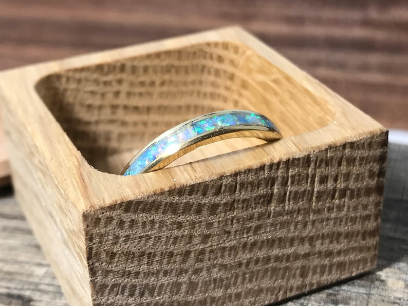 A gold ring with an opal inlay is placed inside a small, open wooden box.
