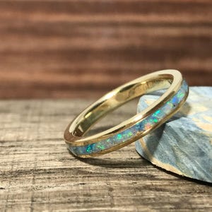 A gold and opal inlay ring is angled next to a blue-green stone piece on wood.