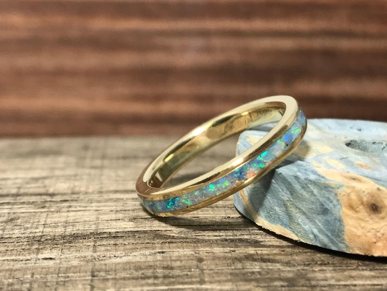 A gold and opal inlay ring is angled next to a blue-green stone piece on wood.