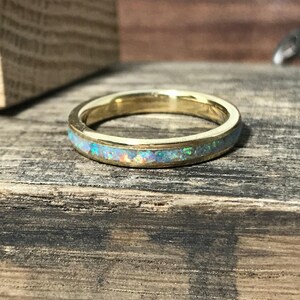 A gold ring featuring an opal inlay lies flat on a dark wooden surface.